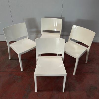 Quatre chaises en plastique blanc sont disposées en cercle sur un sol en briques.