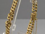 a close up of a gold chain bracelet on a clear stand