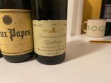 two bottles of wine sitting on a counter next to a cup