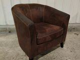 fauteuil club en cuir marron posé sur un sol en béton, devant un mur blanc
