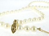 a close up of a white pearl necklace with a gold clasp