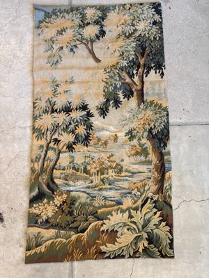 une vieille tapisserie accrochée au mur, représentant une rivière et des arbres