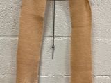 beige scarf with fringes hanging on a hanger against a white brick wall