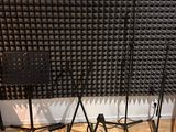 two microphone stands and a chair in front of a sound wall