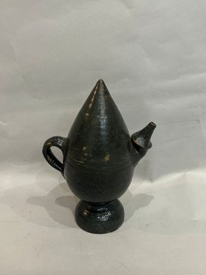 a black vase with a cone shaped handle sitting on a white surface