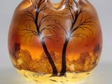 un vase en verre orné d'arbres peints, posé sur une table