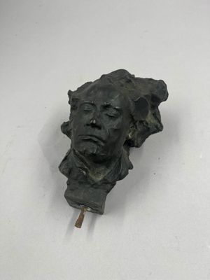 statue représentant la tête d'un homme fixée à un bâton, posée sur une surface blanche