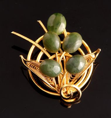 broche plaquée or ornée de jades verts sur un fond noir