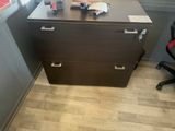 a desk with a file cabinet and a chair in the corner