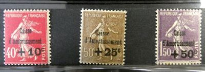 Trois timbres de couleurs différentes sont exposés dans une vitrine.