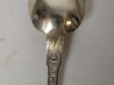a silver spoon with a flower on it on a white surface