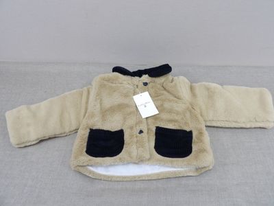 La veste est de couleur beige clair et noire, et comporte une étiquette.