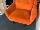 an orange chair sitting in front of a book shelf in a living room