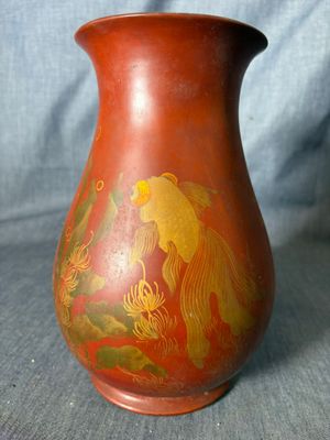 un vase rouge orné de motifs dorés, posé sur un tissu bleu