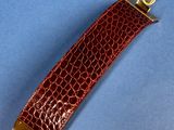 a close up of a brown alligator skin leather strap with a gold clasp