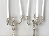 two silver candelabs with white candles on a wooden table
