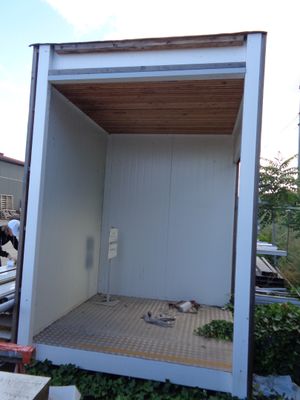 a small white building with a wooden roof in the middle of a yard