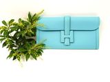 blue leather clutch bag with a plant on a white background