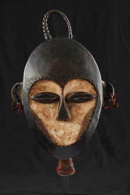 un masque africain posé sur un socle, sur fond noir