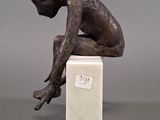 statue of a boy sitting on a marble block with his hands on his knees