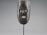 un masque en bois posé sur un socle, devant un fond gris