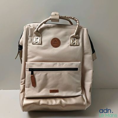 beige backpack sitting on top of a white table next to a white wall