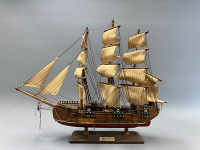 maquette en bois d'un voilier posée sur un socle, sur fond gris