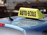 une enseigne « taxi » posée sur le toit d'une voiture, sur laquelle on peut lire « auto-école »