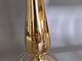 a gold vase on a clear glass plate on a table