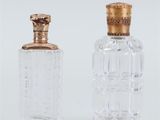 deux bouteilles en verre transparent avec des bouchons dorés, posées sur une surface blanche