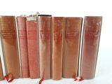 six old books lined up in a row on a white surface
