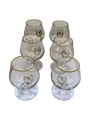 six clear glasses with gold rims are lined up on a white surface