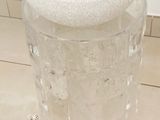 un vase en verre muni d'un couvercle, posé par terre à côté d'un petit sac