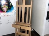 un chevalet en bois sur lequel est posé un tableau, devant une affiche