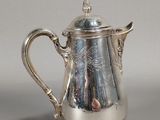 an antique silver coffee pot with a lid on a table
