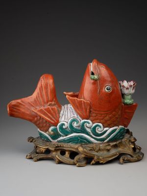 une photo représentant une statue de poisson rouge et vert posée sur un socle en bois
