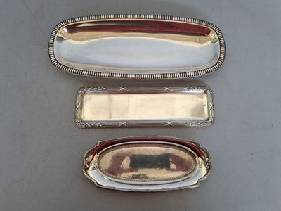 trois plateaux rectangulaires en métal argenté, munis de poignées, posés sur une table