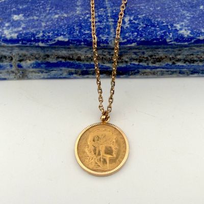 a gold coin necklace sitting on top of a blue stone