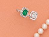 un gros plan sur un collier de perles accompagné d'une bague sertie d'une émeraude et de diamants