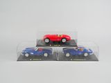 trois petites voitures rouges et bleues dans des boîtes transparentes, posées sur une surface blanche