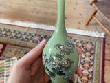 a person holding a green vase on a table