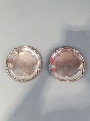une paire de dessous de verre plaqués argent posés sur une table, avec l'ombre d'une personne en arrière-plan