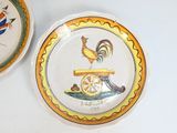 une assiette sur laquelle est représenté un coq, à côté d'une assiette sur laquelle est représenté un oiseau