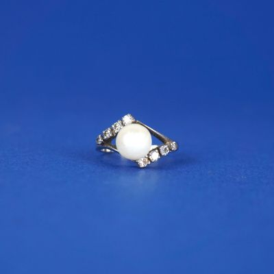 une bague en perle blanche et diamants sur fond bleu