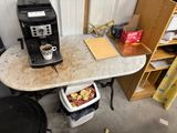 a coffee maker sitting on top of a table next to a trash can