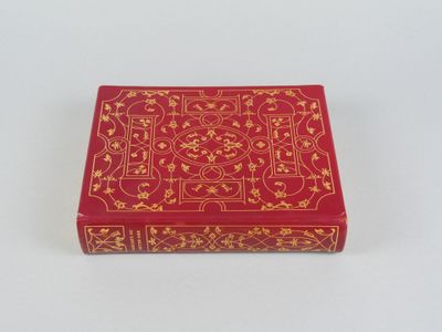 une boîte rouge ornée de motifs dorés, posée sur une surface blanche