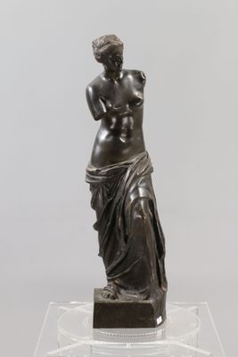 une statue en bronze représentant une femme tenant un bébé dans ses bras, posée sur un socle transparent