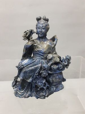 a statue of a woman sitting on a rock with a bird in her hand