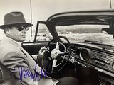 photographie en noir et blanc d'un homme assis dans une voiture, coiffé d'un fedora