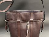 brown leather purse with tassel and strap on grey background